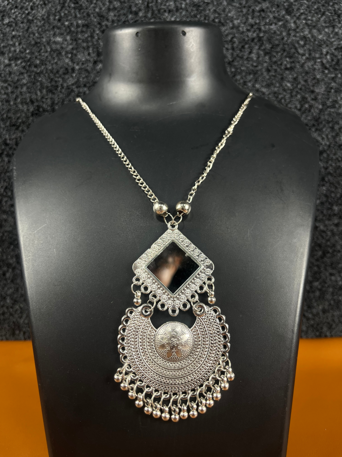 Oxidized silver mirror pendant necklace featuring a bold square and circular pendant with intricate detailing, displayed on a black mannequin.