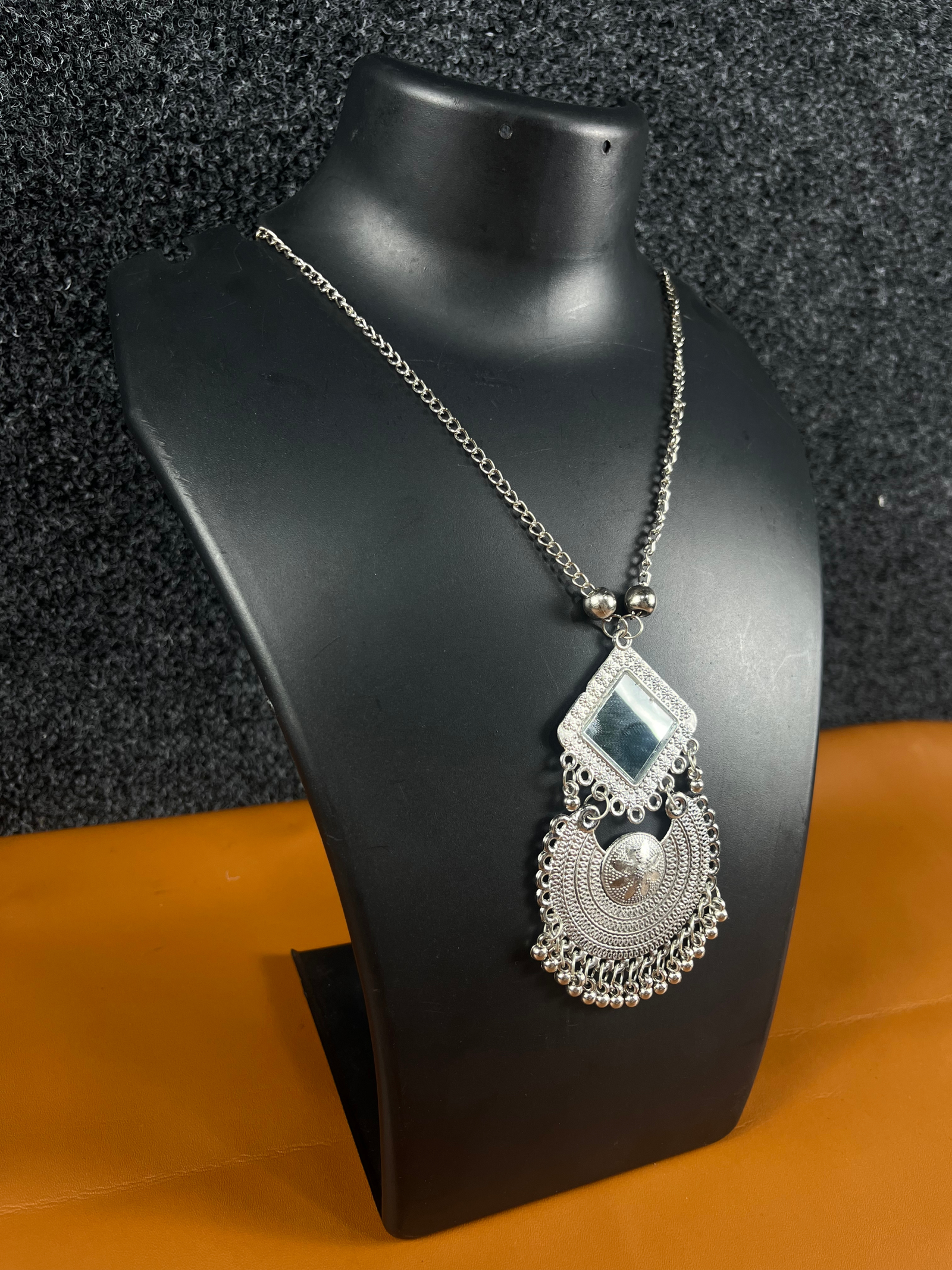 Oxidized silver mirror pendant necklace featuring a bold square and circular pendant with intricate detailing, displayed on a black mannequin.