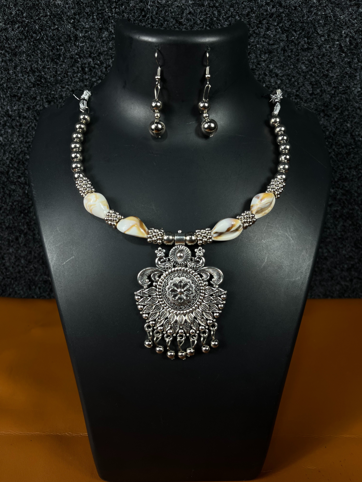 Oxidized silver floral pendant necklace set with matching drop earrings displayed on a black stand, perfect for ethnic and festive wear.